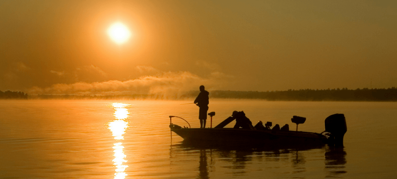 Silhouette of people fishing from a powerboat, with bright orange sun over lake