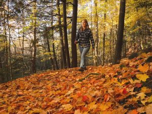A woman walks along a trail covered in autumn leaves