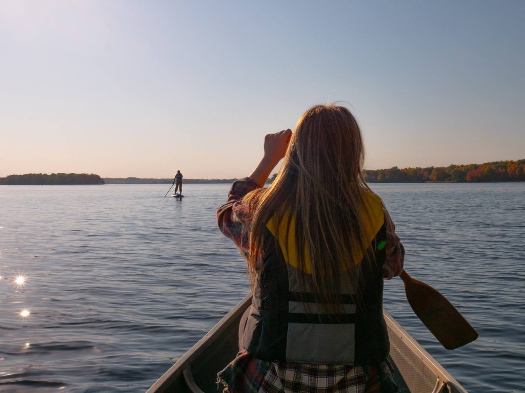 A person paddles a canoe on a fall day