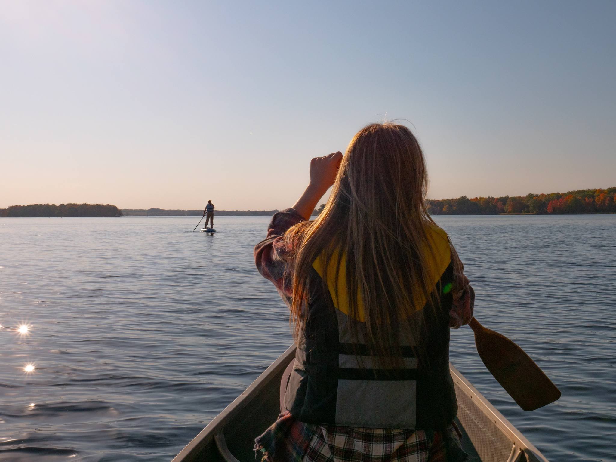 A person paddles a canoe on a fall day