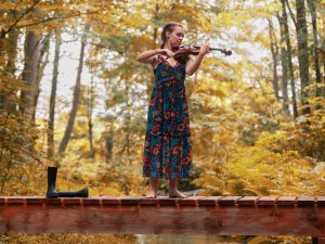 A violin player stands on a footbridge in fall