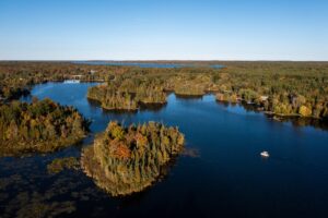Aerial view of lake surrounded by fall forest, with a boat visible below