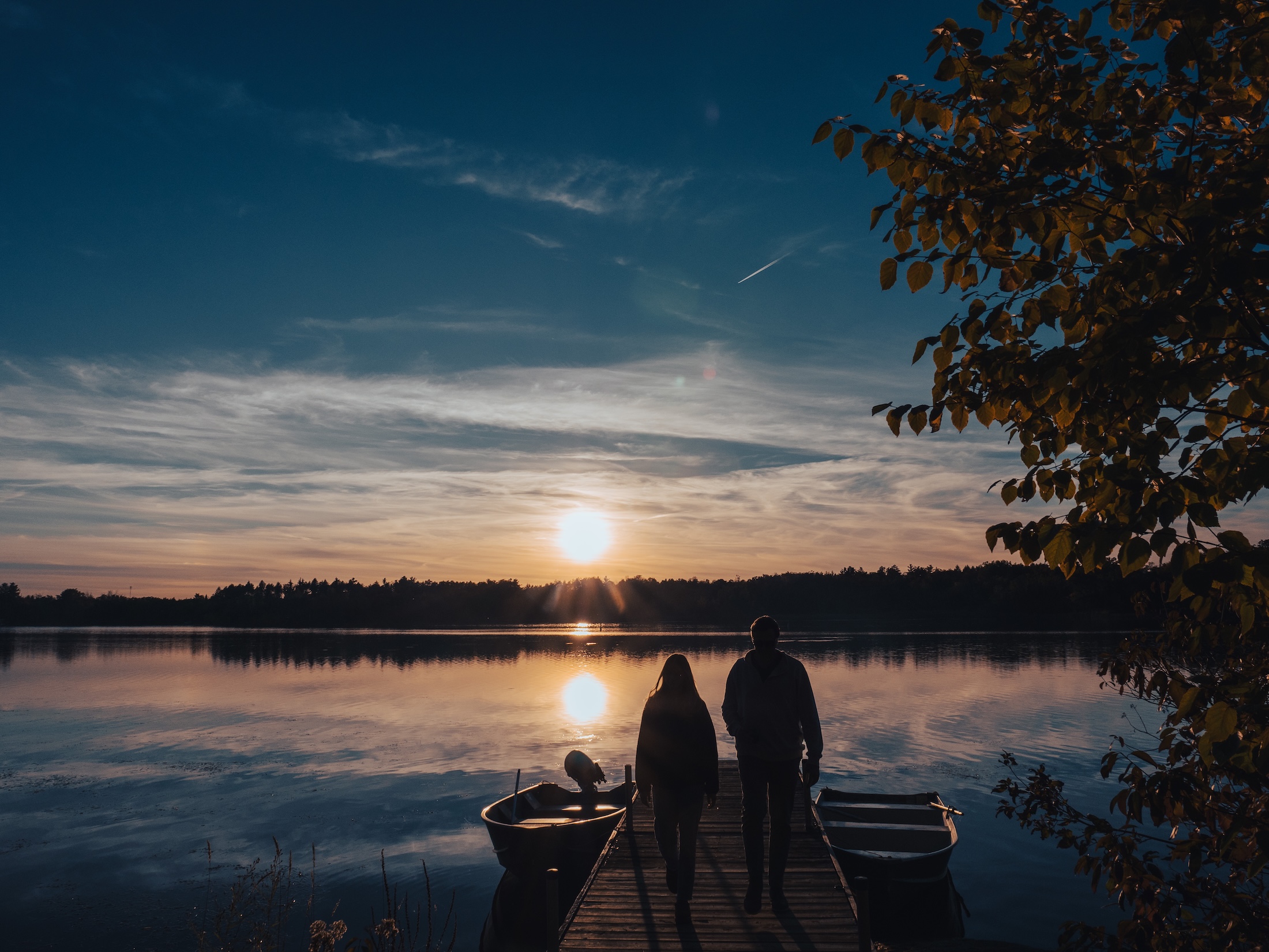 Scan My Site Free See how it works Click to select or drop a new image Use setting Optional Two people walk on a dock toward a calm lake at sunset, with boats on either side and a tree with yellow leaves on the right.