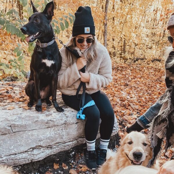 Girl with a toque sitting in the woods with a black dog, golden retriever is at her feet